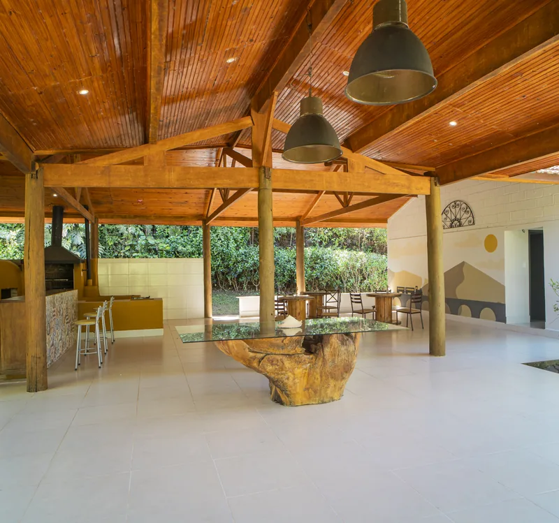 Área gourmet com mesas de madeira, cobertura e jardim ao redor