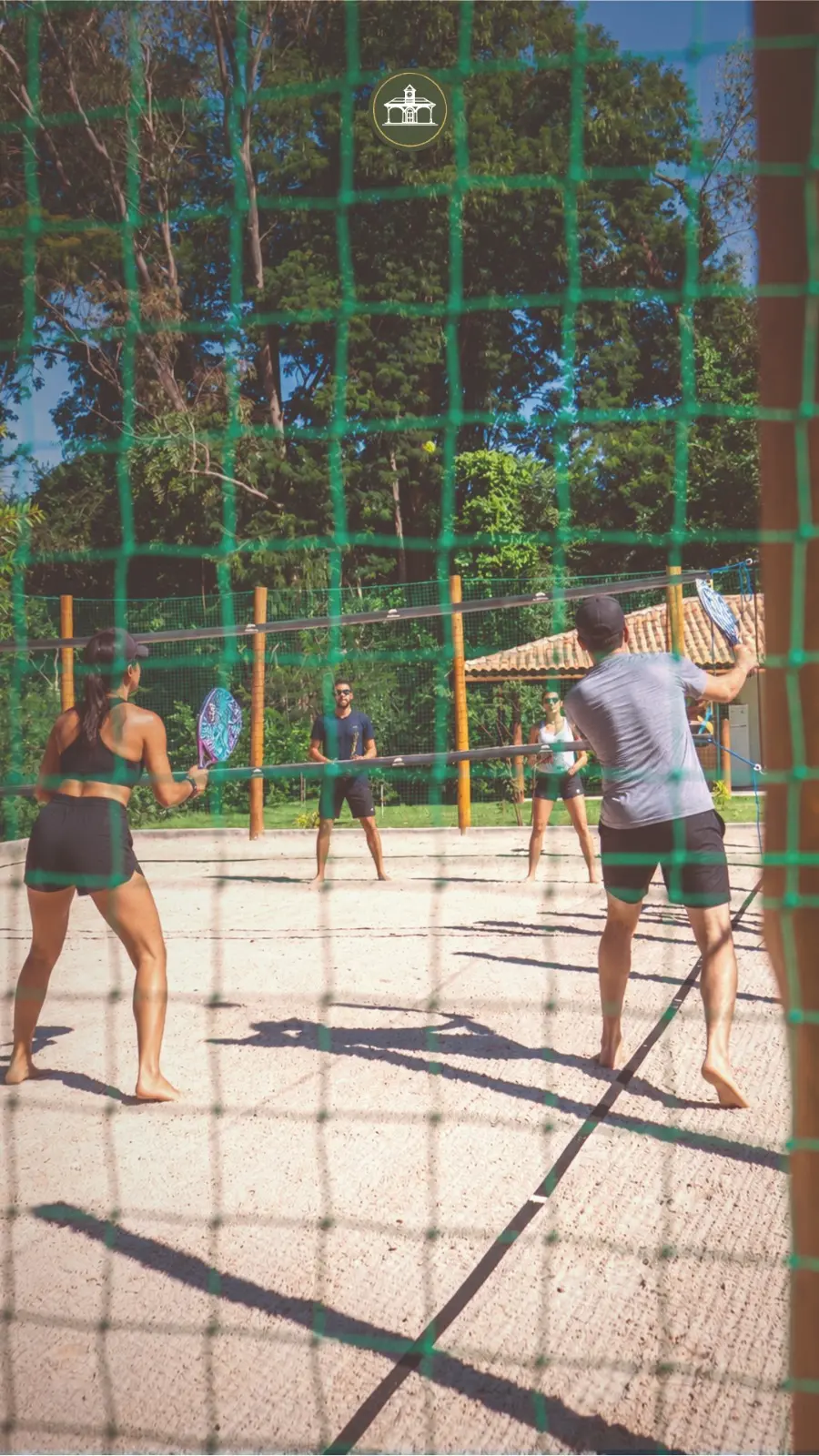 Pessoas jogando beach tennis em meio ao verde
